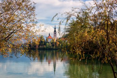 Slovenya 'daki ünlü Alp Bled Gölü (Blejsko jezero), muhteşem sonbahar manzarası. Gölün manzarası, kiliseli ada, bulutlu mavi gökyüzü ve sudaki yansıma, dış seyahat arka planı.