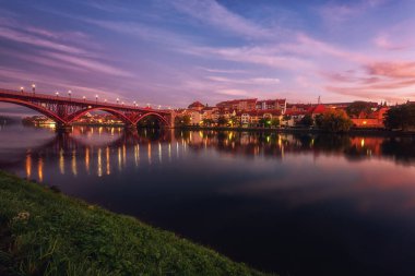 Slovenya 'nın başkenti Drava nehrinin kıyısındaki Maribor Eski Köprüsü' nün (Stari Most) muhteşem manzarası. Dramatik bulutlu gökyüzü ve yansıması olan manzaralı şehir manzarası, dış seyahat arka planı