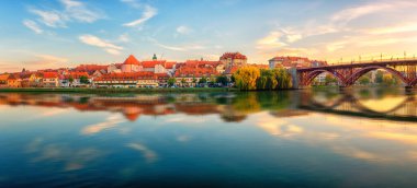 Amazing view of Maribor Old city, Main bridge (Stari most) on the Drava river at sunrise, Slovenia. Scenic cityscape with blue sky and reflection, travel background for wallpaper or guide book clipart