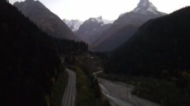 Akşam dağları, yol ve ormanlar, geçen arabalar ve nehir manzarası. Dombay, Rusya. İHA