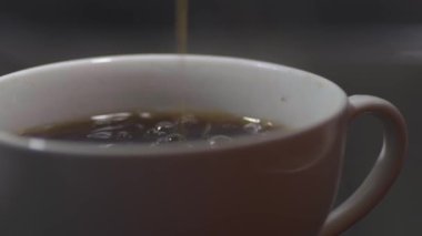 Taze demlenmiş kahve koyu arkaplanda beyaz bir fincana dökülür. Yakın çekim, makro