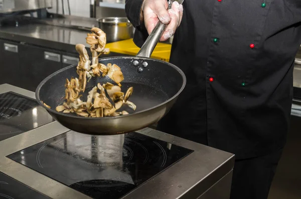 Aşçı tavada mantar kızartıyor, fırlatıyor ve ters çeviriyor. Yemek pişirme süreci