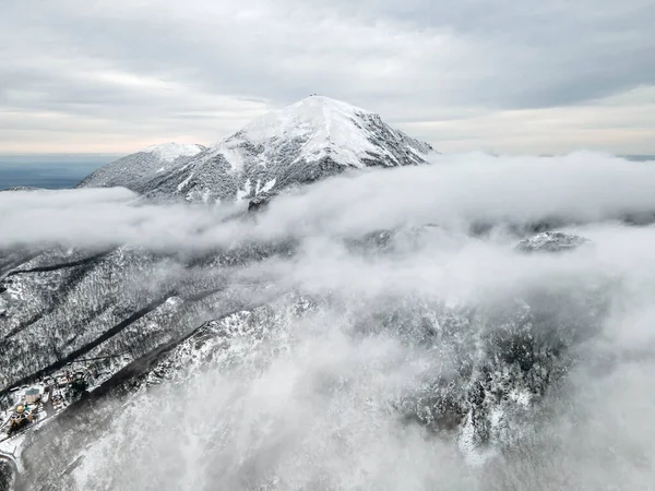 Kar altındaki dağ zirvesi alçak bulutların arka planına karşı. Pyatigorsk Dağı, Beshtau Dağı.
