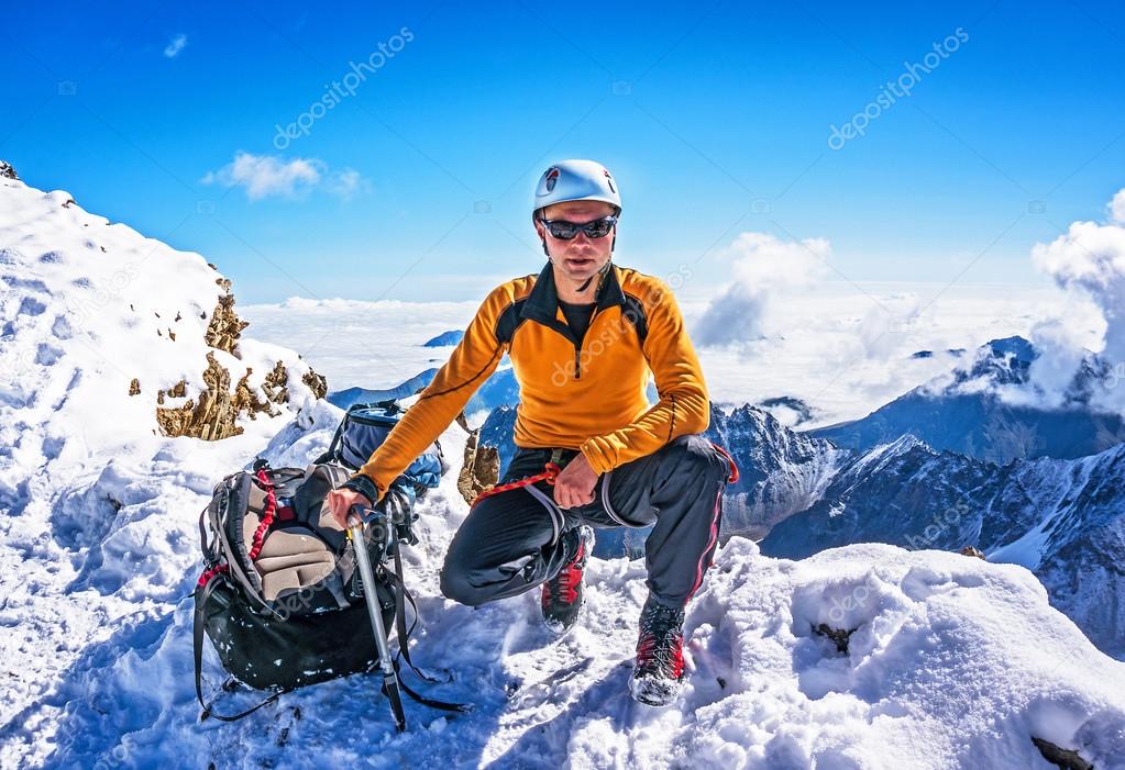 Climber on a mountain top posing on the background of snowy mountains
