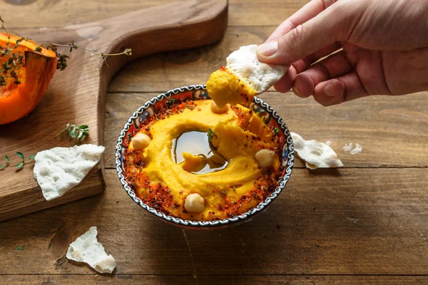 L'homme tremper du pain dans le houmous de citrouille sur un fond de bois sombre. le tonifiant. focus sélectif — Photo