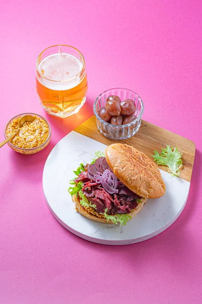 Hamburguesa Pastrami con mostaza, cerveza y pepinillos sobre fondo rosa brillante — Foto de Stock