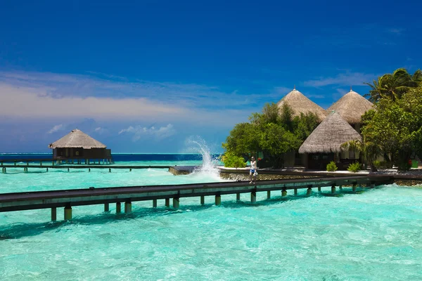 Chica camina sobre un puente de madera que conduce a un bungalow en el Maldi Imagen De Stock