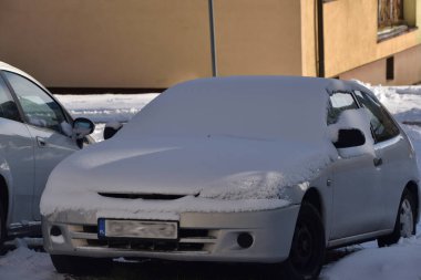 Karla kaplı bir araba, bir otoparkta duruyor.      