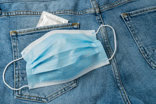 Condom and medical mask on blue jeans background. Healthcare and all-round protection concept.