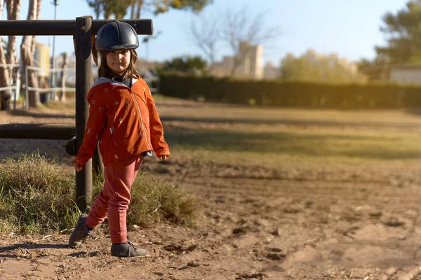 4 year old girl in horse riding dressed and ready to ride with nice posture and sunbeam. environment mixed between rural and urban