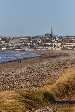 Arka planda şehir olan İrlanda plajı ve dağın tepesinde Katolik kilisesi. Tramore doğa rezervi. Waterford. İrlanda. dikey biçim