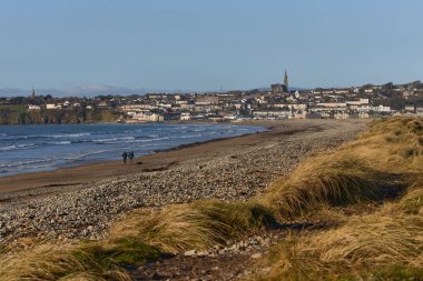 Arka planda şehir olan İrlanda plajı ve dağın tepesinde Katolik kilisesi. Tramore doğa rezervi. Waterford. İrlanda. manzara