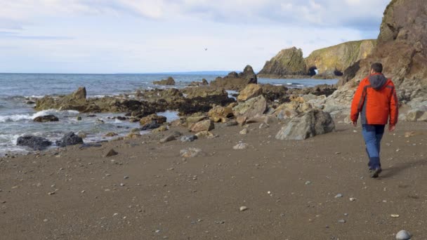 Un hombre sentado en la playa de rocas en una playa Kilfarrasy. — Vídeos de Stock