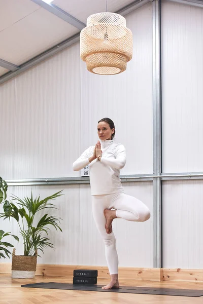 Yoga hocası iyi dekore edilmiş bir spor salonunda karmaşık bir duruş öğretiyor..