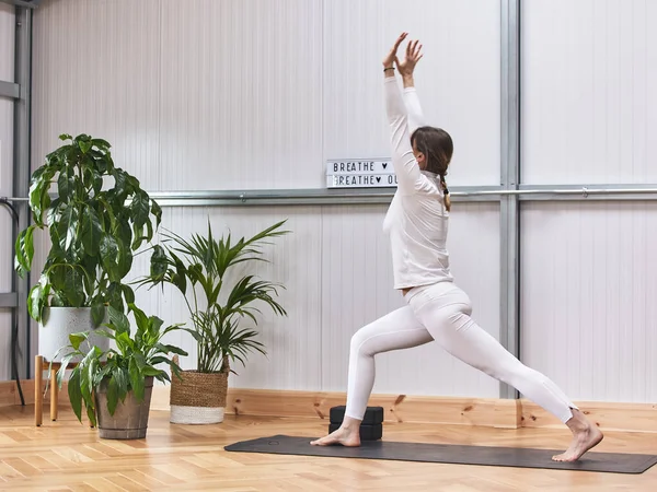 İnce Rus kız yoga yaparken asana minderin üzerinde duruyor. Savaşçı 'nın içinde duran barışçıl odaklı kız. Virabhadrasana pozu, beyaz spor giysi. Stres yok..
