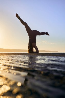 Yoga eğitimi ve meditasyon şafakta ya da alacakaranlıkta sahilde poz vermek. Kadın yoga, dingin okyanus manzarasında egzersiz yapıyor. Güneşe karşı bir kadın gibi siluet.