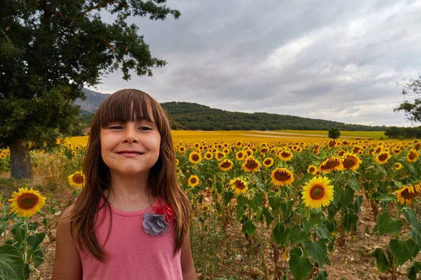 Mädchen mit lustigem Gesicht, das in einem atemberaubenden Sonnenblumenfeld in die Kamera blickt — Stockfoto