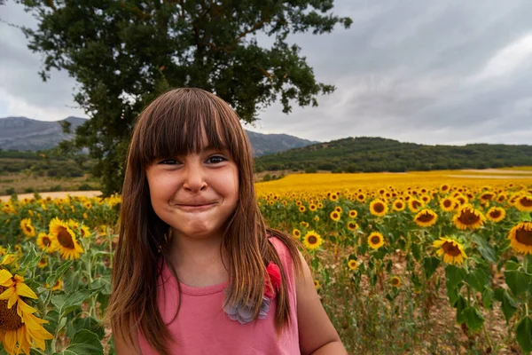 Meisje met grappig gezicht, kijken naar camera in een prachtig veld van zonnebloemen. — Stockfoto