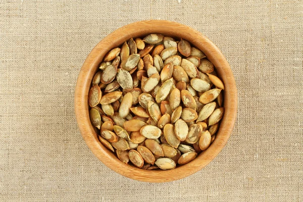 Shelled  roasted pumpkin seeds in bamboo bowl on rough linen cloth — Stock Photo, Image