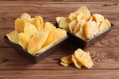 Kurumuş mango parçaları ve kahverengi bir seramik kasenin üzerinde ahşap bir masada duran meyveler. Makro. Yakın çekim.