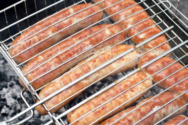 Izgara ızgaralarının arasına sıkıştırılmış et sosisleri ızgarada kızartılıyor. Yakın çekim.