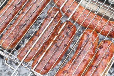 Izgara ızgaralarının arasına sıkıştırılmış et sosisleri ızgarada kızartılıyor. Yakın çekim.