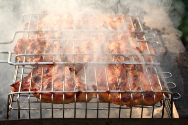 Izgara ızgaralarının arasına sıkıştırılmış tavuk parçaları ızgarada kızartılıyor. Yakın çekim.