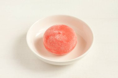 Beyaz ahşap bir masada küçük beyaz bir kase üzerinde ballı Japon tatlı mochi ile nar. Kapatma