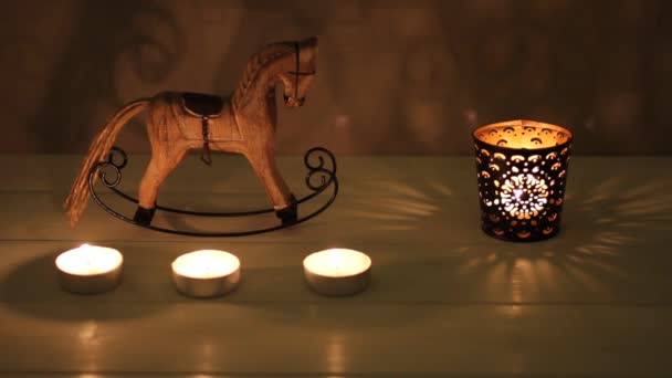 Christmas decoration - wooden toy rocking-horse and candle in candlestick on white wooden table against concrete wal — Stock Video