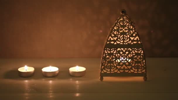 Пылающие свечи и свечи в подсвечнике на белом деревянном столе напротив бетонной стены — стоковое видео
