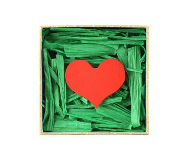 Red painted wooden heart enclosed with green paper raffia strips in beige box isolated on white background