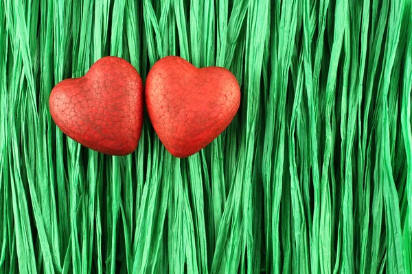 Two red painted polyfoam hearts on green paper raffia strips background — Stock Photo, Image