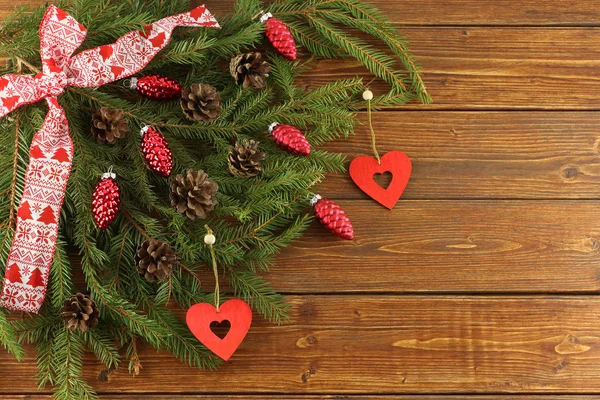 Ghirlanda di Natale - coni rossi e cuori rossi di legno su rami di abete rosso verde su sfondo di legno marrone — Foto Stock