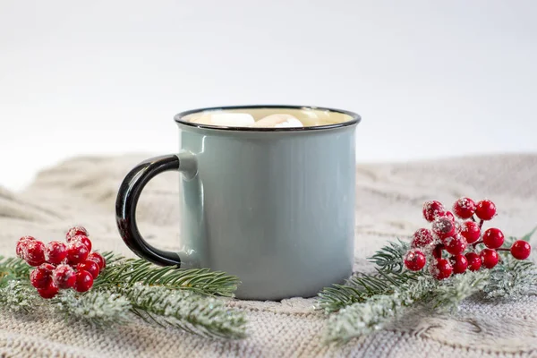 İştah açıcı kokulu kupa marşmelovlu ve sıcacık örülü arka planda bir Noel filizli kakao.