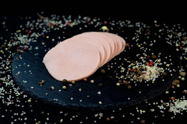 Chutné klobásy krájené na břidlicové desce na černém pozadí s kořením a chilli, selektivní umělecké zaměření — Stock fotografie