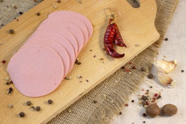 İştah açıcı sosis, pürüzlü keten arka planda, acı biber ve baharatlı sarı bir tabakta dilimlenmiş, yakın plan.