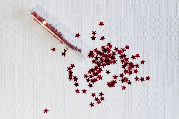 Pailletten Röhre verstreut rote Sterne glitzern auf weißem strukturierten Hintergrund Nahaufnahme — Stockfoto