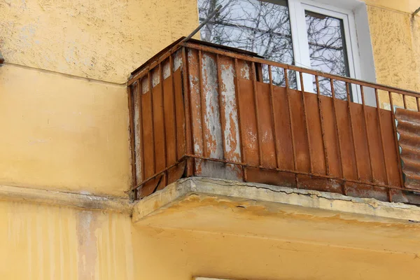Parlak sarı bir duvarda eski paslı balkon, tehlikeli hasar.