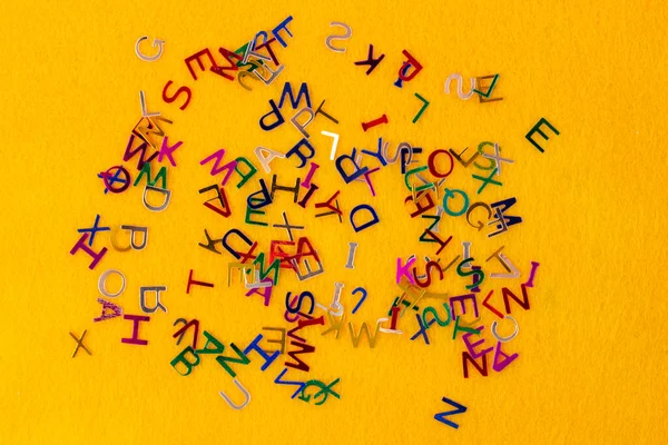 Pequeñas letras multicolores brillantes esparcidas sobre un fondo naranja —  Fotos de Stock