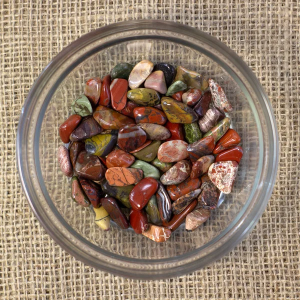 Κόκκινο και πολύχρωμα ίασπη γυαλισμένο tumblestones σε γυάλινο πιάτο σε τραχύ λινό φόντο — Φωτογραφία Αρχείου