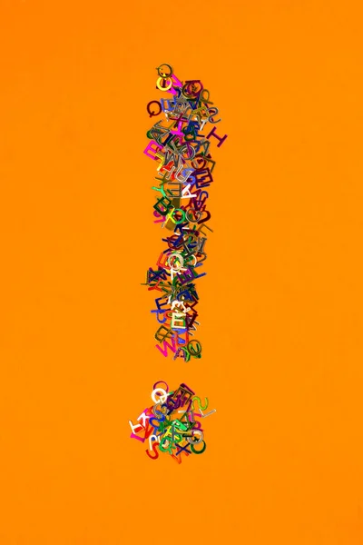 Petites lettres multicolores brillantes éparpillées forme point d'exclamation sur fond orange — Photo