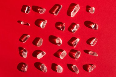 Jeolojik koleksiyondaki doğal mineral örnekleri - kırmızı zeminde yuvarlanmış renksiz kaya kristal taş