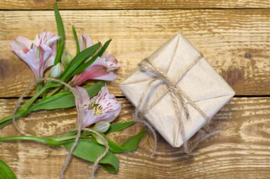 Parlak beyaz ve pembe çiçekler, Alstroemeria ve el işi kağıt, ahşap desenli arka plan üzerine sarılı hediye paketi.