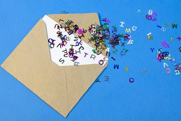 Простий крафт-паперовий конверт з розкиданими яскравими кольоровими дрібними літерами крупним планом — стокове фото