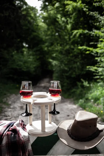 pair of wine goblets and cowboy hat on the barrier in the reserve. Picnic in nature.