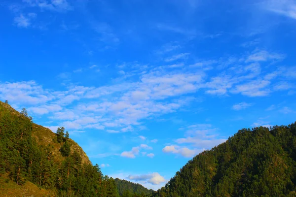 Ciel bleu vif avec des nuages blancs. Les sommets verts des montagnes. — Photo