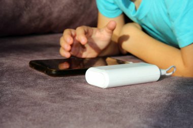 Çocuk elinde telefonla gri bir kanepede yatıyor..