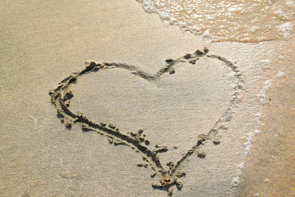 Kalp plaj kum üzerine çizilmiş. dalga deniz tarafından yıkanmış kum kalp sembolü.
