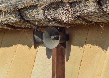 Vintage horn loudspeakers on a wall under a thatched roof. Horn speaker. clipart