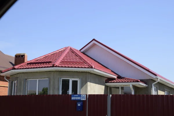 A house with a roof made of metal sheets. The house with gables, windows and metal roof, equipped with overflow and protection from snow.